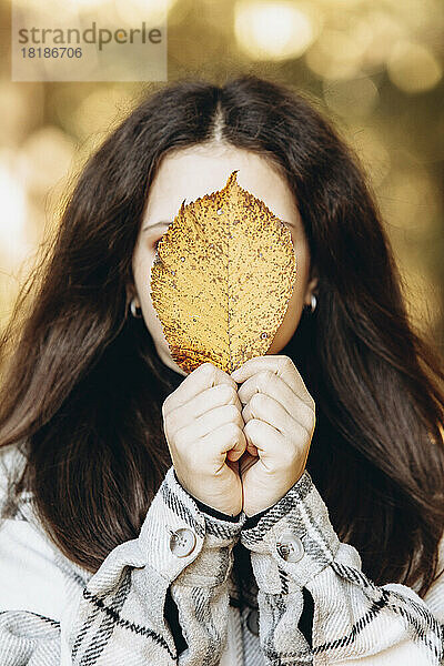 Mädchen bedeckt Gesicht mit gelbem Blatt