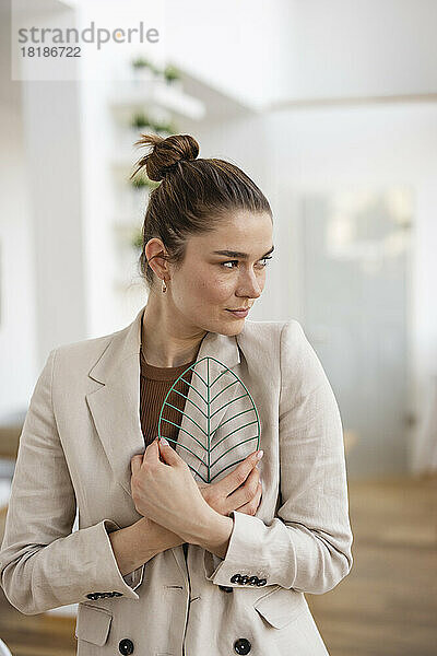 Geschäftsfrau umarmt blattförmiges Modell im Büro