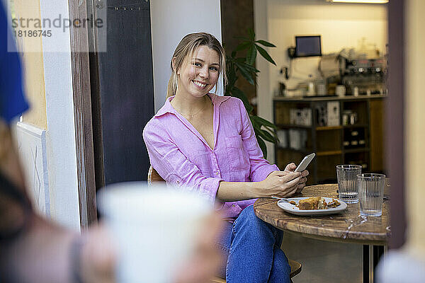 Glückliche blonde Geschäftsfrau sitzt mit Smartphone am Tisch im Café