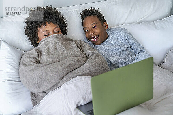 Mutter und Sohn verbringen ihre Freizeit mit einem Laptop  der zu Hause im Bett liegt