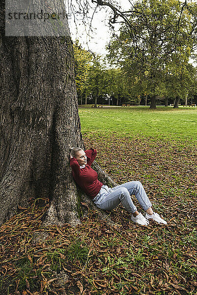 Junge Frau entspannt sich am Baum im Park
