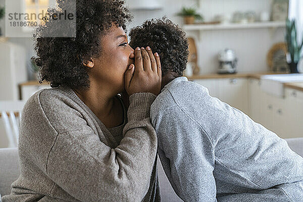 Mother whispering in son's ear at home