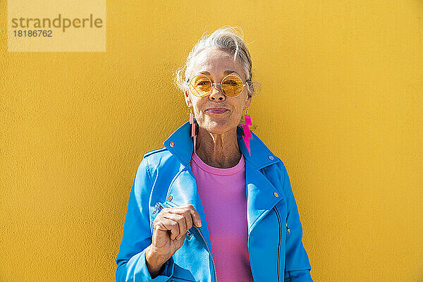 Lächelnde reife Frau mit Sonnenbrille vor gelber Wand