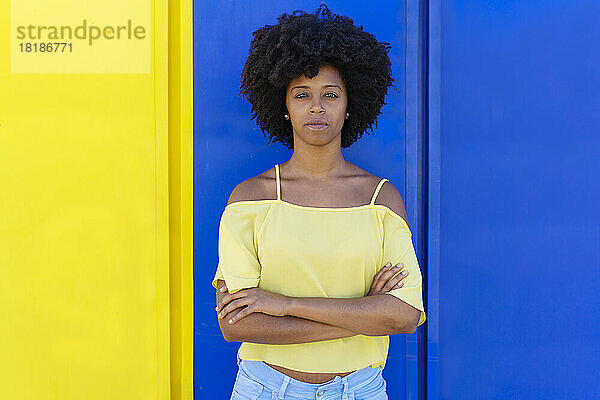 Selbstbewusste junge Frau steht mit verschränkten Armen vor einer zweifarbigen Wand