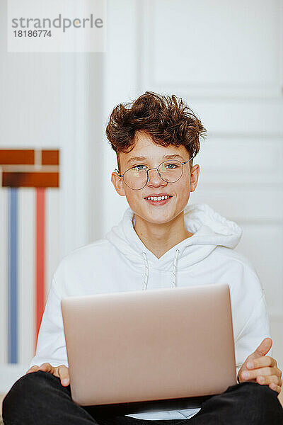 Lächelnder Junge sitzt mit Laptop zu Hause
