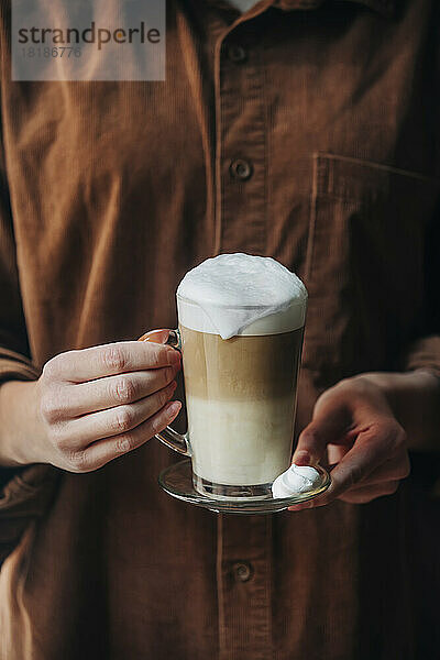 Hände einer Frau  die ein Glas Cappuccino hält