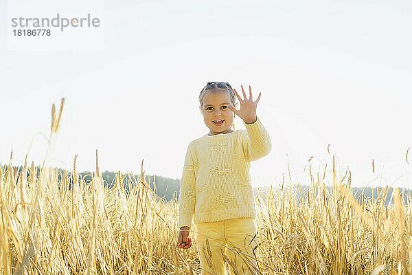 Fröhliches süßes Mädchen gestikuliert und steht an einem sonnigen Tag auf dem Feld