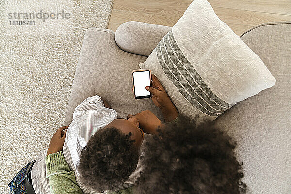 Mutter und Sohn mit Handy liegen zu Hause auf dem Sofa