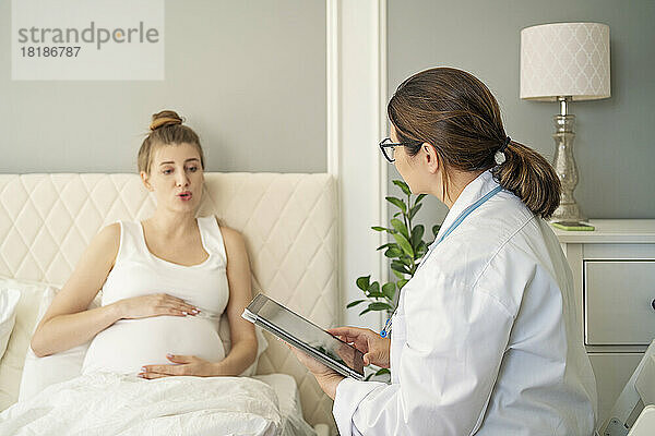 Arzt spricht zu Hause mit schwangerer Frau im Bett
