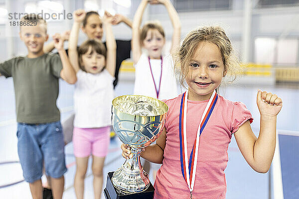 Mädchen mit Medaille und Trophäe feiert Sieg mit Freunden auf dem Schulsportplatz