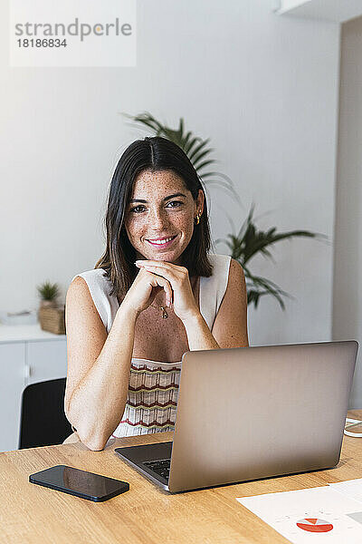 Glückliche junge Geschäftsfrau  die im Büro vor dem Laptop sitzt