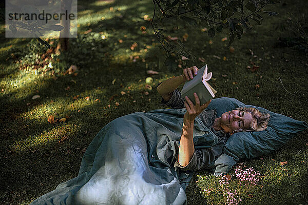 Reife Frau liest Buch im Garten liegend