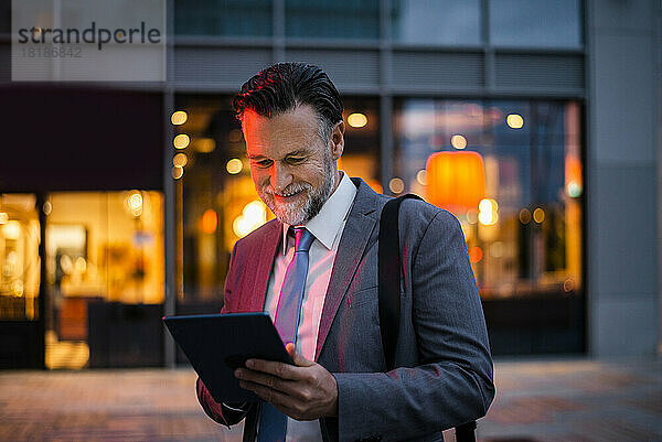 Lächelnder reifer Geschäftsmann mit Tablet-PC auf Fußweg