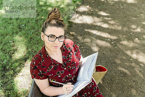 Porträt einer Frau  die auf einer Bank sitzt und in ein Notizbuch schreibt