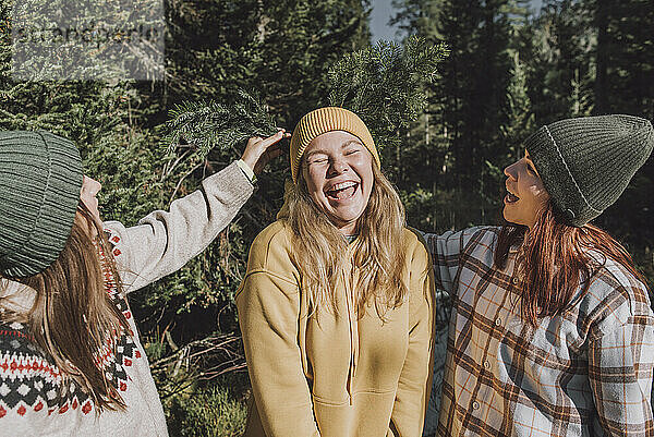 Frauen stecken einen Fichtenzweig in die Strickmütze einer glücklichen Freundin im Wald