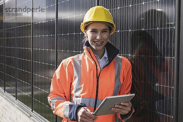 Glückliche Ingenieurin mit Tablet-PC  der sich auf Sonnenkollektoren stützt