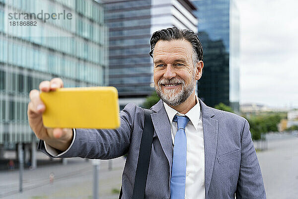 Glücklicher reifer Geschäftsmann  der vor dem Gebäude ein Selfie mit dem Smartphone macht