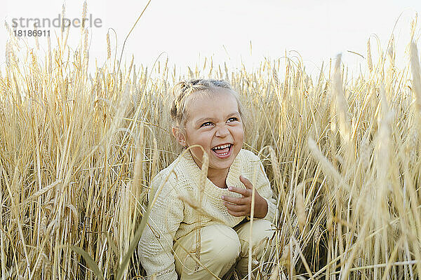 Fröhliches Mädchen kauert inmitten von Feldfrüchten