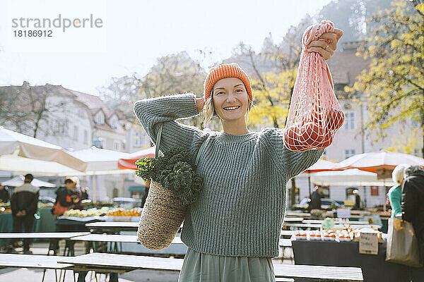 Lächelnde Frau zeigt Tomaten im Netzbeutel auf dem Markt