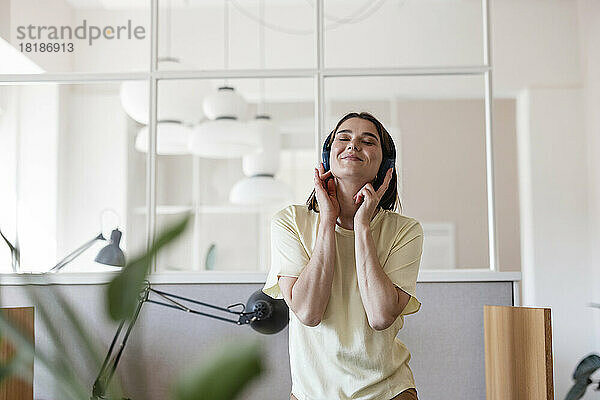 Geschäftsfrau mit geschlossenen Augen genießt Musik und hört im Büro über kabellose Kopfhörer