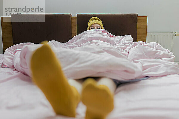 Junge Frau mit Decke entspannt sich zu Hause im Bett
