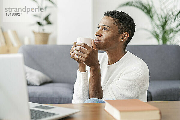 Nachdenkliche Frau hält eine Tasse Kaffee im liebevollen Zimmer zu Hause