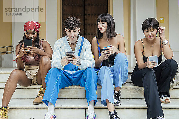 Fröhliche Freunde nutzen Smartphones auf der Treppe vor der Tür