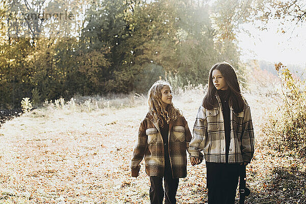 Girl holding hands with sister and walking in forest on sunny day