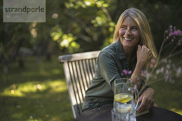 Glückliche reife Frau mit blonden Haaren sitzt im Garten