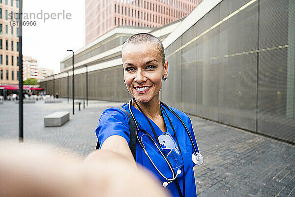 Lächelnder reifer Mitarbeiter im Gesundheitswesen  der ein Selfie auf dem Fußweg macht