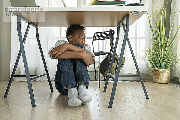 Gestresster Junge sitzt zu Hause unter dem Tisch