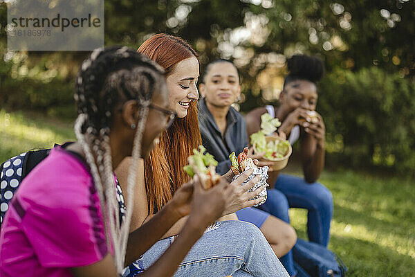 Lächelnde junge Frau mit Freunden  die im Park einen Snack essen