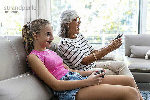 Großmutter und Enkelin genießen es  zu Hause auf dem Sofa Videospiele zu spielen