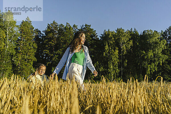 Glückliche Frau  die an einem sonnigen Tag mit ihrer Tochter im Feld spaziert