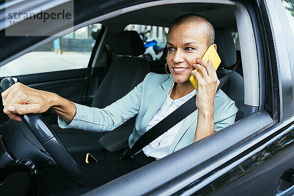 Lächelnde Geschäftsfrau  die im Auto mit dem Smartphone spricht