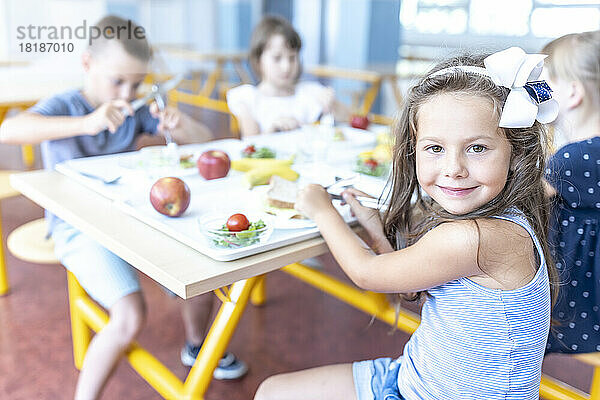 Smiling girl having lunch with friends sitting at table in school cafeteria