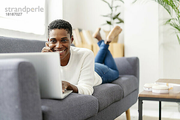 Smiling woman lying on couch using laptop