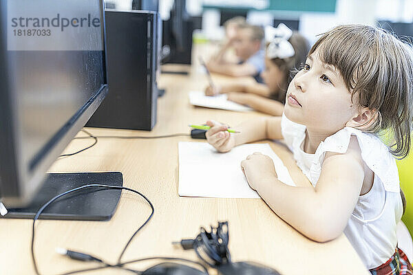 Grundschülerin schaut im Klassenzimmer auf den Desktop-Bildschirm
