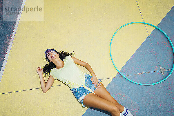 Happy woman lying by hoop on sports court