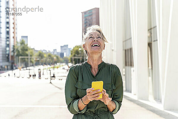 Reife Frau mit Smartphone lacht an sonnigem Tag