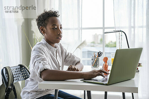 Junge macht Hausaufgaben mit Laptop zu Hause