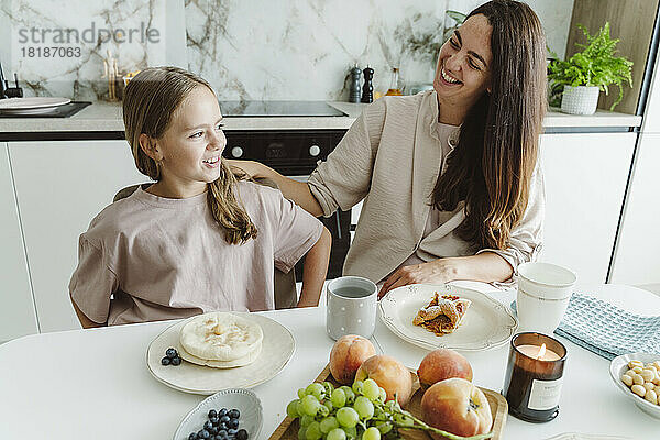 Glückliche Frau mit Tochter am Esstisch in der Küche