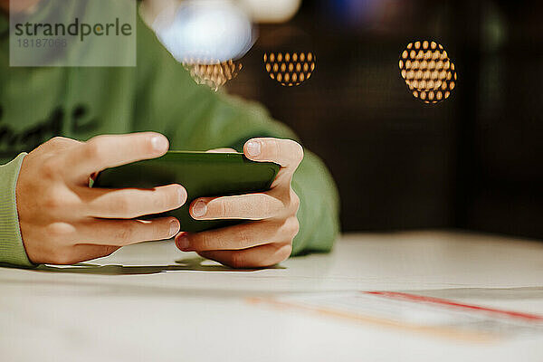 Hände eines Jungen  der sein Smartphone am Tisch im Food-Court benutzt