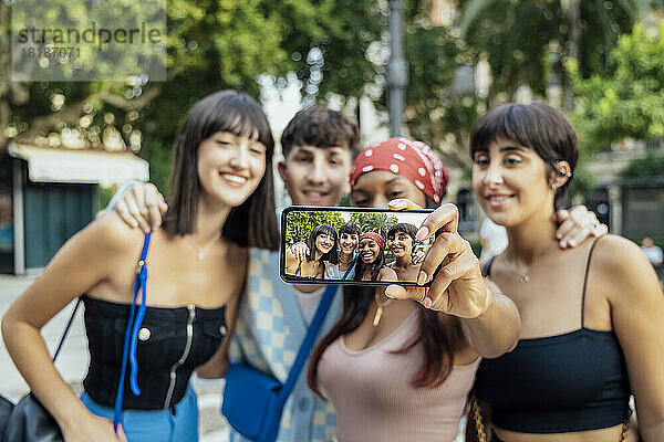 Frau zeigt ihr Selfie auf dem Handy mit Freunden im Park