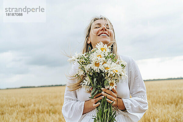 Lächelnde Frau steht mit einem Strauß weißer Blumen vor dem Himmel