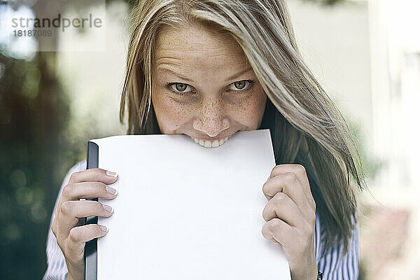 Germany  Duesseldorf  Young woman biting folder  portrait