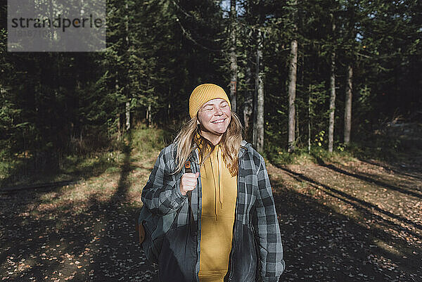 Glückliche Frau mit geschlossenen Augen beim Wandern im Wald an einem sonnigen Tag