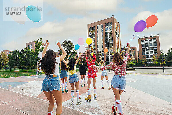 Freunde halten bunte Luftballons beim Rollschuhlaufen auf dem Sportplatz