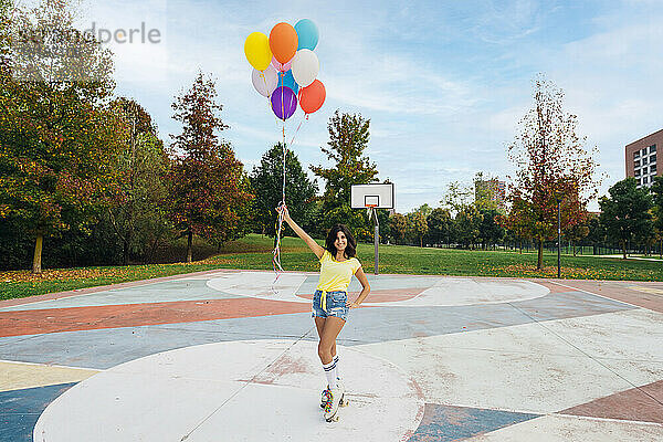 Lächelnde Frau mit Rollschuhen und bunten Luftballons auf dem Sportplatz