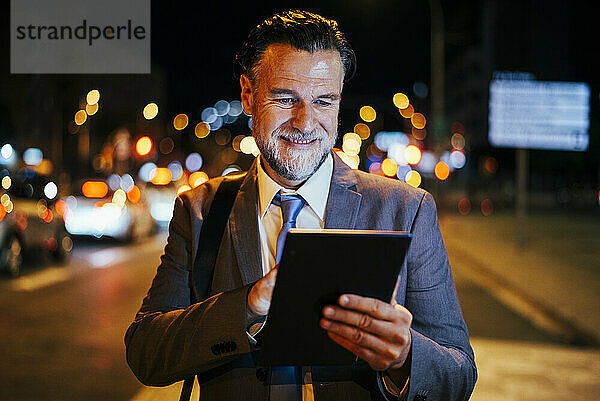 Glücklicher reifer Geschäftsmann  der nachts einen Tablet-PC nutzt